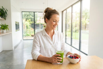 Femme souriante qui prend un jus vert et des baies pour une meilleure vitalité