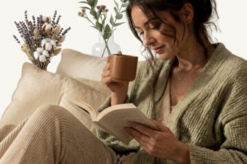 Femme détendue en gilet, lisant un livre avec une tasse à la main, rituel bien-être du soir